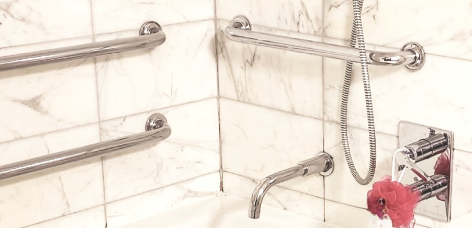 Image: My hotel bath/shower combo in NY, complete with grab bars and a removable showerhead. My pink pouf and prosthetic liner are in also in view.