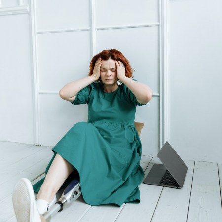 Image: Woman wearing a prosthetic who is holding her head as if stressed. Source: Thirdman/Pexels.com