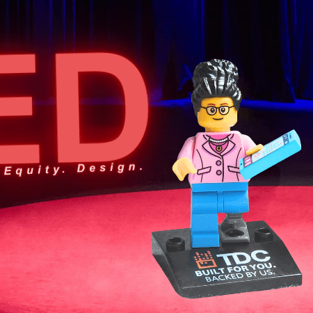 LEGO figure of a woman with a cell phone and prosthetic leg standing on a red stage under the word RED, which stands for Representation, Equity, Design.