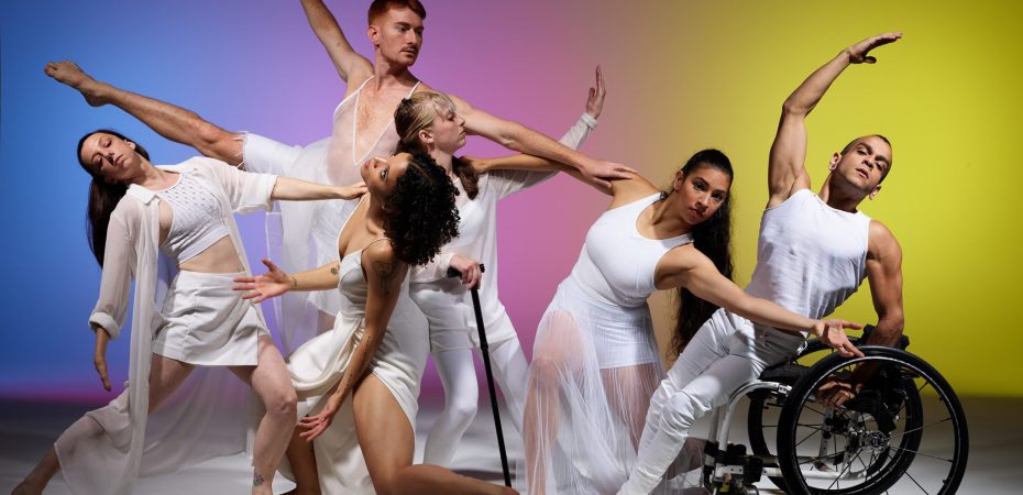 Six professional dancers from Axis Dance Company perform in flowing white costumes against a colorful gradient background. The dancers include both disabled and non-disabled performers - one dancer uses a wheelchair, another uses a crutch, while others are standing or in dynamic poses with arms extended. All are dressed in elegant white flowing garments, demonstrating the grace and artistry of inclusive contemporary dance.