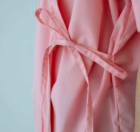 Close-up of the back tie on a pink hospital gown, highlighting the thin fabric and knot.