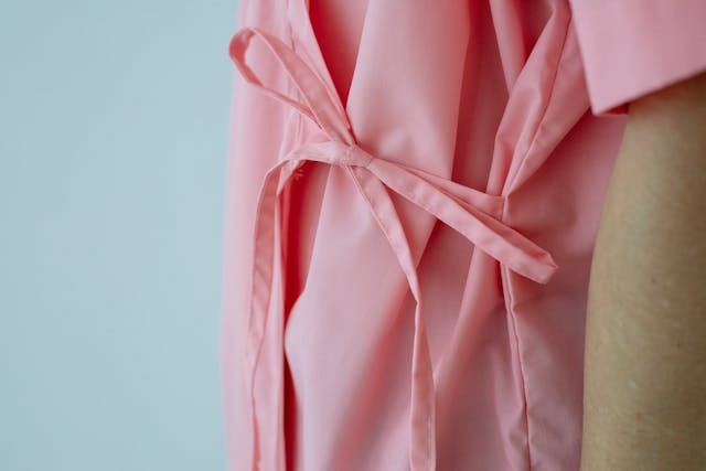 Close-up of the back tie on a pink hospital gown, highlighting the thin fabric and knot.
